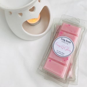 May include: A pink soy wax melt in a clear plastic packaging with a white label that says "The Cosy Scent Shack Soap & Glory Soy Wax Melts HANDMADE".
