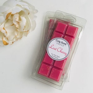 May include: A stack of three clear plastic containers with a pink soy wax melt inside. The wax melt is labelled "The Cosy Scent Shack Lost Cherry" and "Soy Wax Melts Handmade".