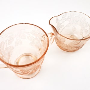 May include: A set of two vintage pink glass sugar and creamer bowls with floral designs. The bowls have a delicate, feminine look and are perfect for adding a touch of elegance to any table setting.