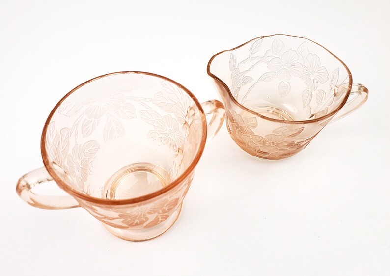 May include: A set of two vintage pink glass sugar and creamer bowls with floral designs. The bowls have a delicate, feminine look and are perfect for adding a touch of elegance to any table setting.