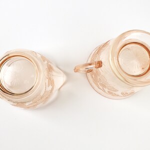 May include: A set of two vintage pink glass creamer and sugar bowls with a floral design. The bowls have a delicate, feminine look and are perfect for adding a touch of elegance to any table setting.