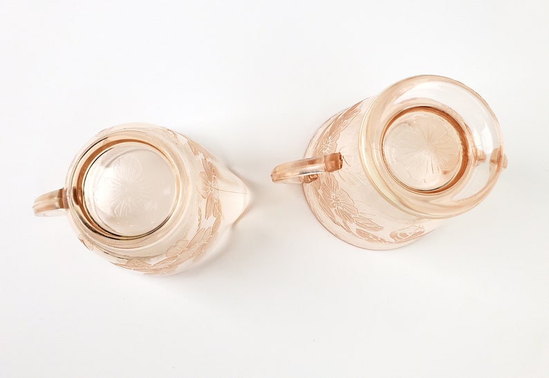 May include: A set of two vintage pink glass creamer and sugar bowls with a floral design. The bowls have a delicate, feminine look and are perfect for adding a touch of elegance to any table setting.