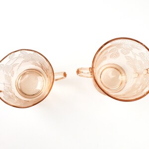 May include: A set of two vintage glass creamer and sugar bowls with a floral design. The bowls are made of pink glass and have a delicate etched pattern.