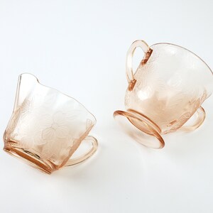 May include: A set of two vintage glass creamer and sugar bowls with a floral design in a pale pink color.