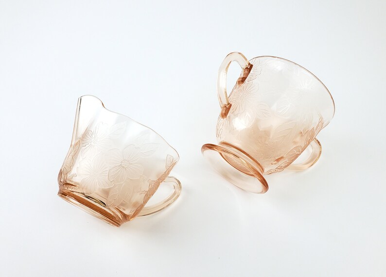 May include: A set of two vintage glass creamer and sugar bowls with a floral design in a pale pink color.