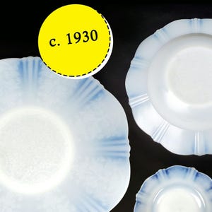 May include: A selection of vintage white and pale blue glass plates. The plates feature a ruffled edge design and a floral pattern. The text "c. 1930" is displayed in a yellow circle.