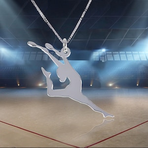 May include: Silver necklace featuring a pendant shaped like a gymnast performing a routine. The pendant is detailed and shows the gymnast in mid-air with a ribbon.