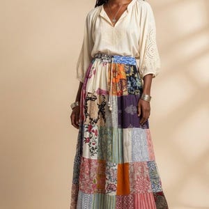 May include: A woman wearing a cream-colored blouse with embroidered details and a long, patchwork skirt. The skirt features a variety of colorful fabric patterns. The outfit is bohemian in style.