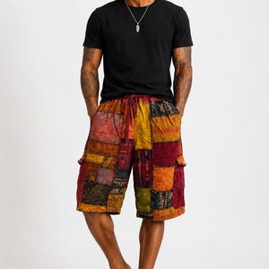 May include: A black short-sleeved t-shirt with a silver feather pendant necklace and knee-length patchwork shorts featuring a variety of colorful fabric squares in shades of red, orange, yellow, and brown with a drawstring waist and tan sandals.