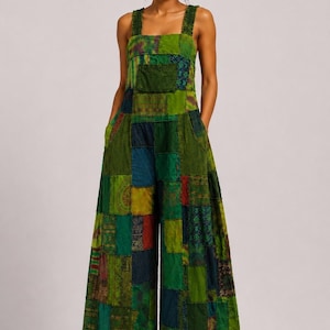 May include: A sleeveless jumpsuit featuring a patchwork design with various shades of green, blue, and dark red fabric squares. The garment has wide legs, a square neckline, thick shoulder straps, and a single chest pocket on the front bodice.
