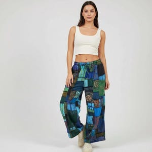 May include: A sleeveless white crop top paired with wide-leg trousers featuring a patchwork design in various shades of blue and green. The pants have a drawstring waist and are constructed from multiple fabric panels with diverse patterns.