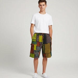 May include: A person wearing a white t-shirt and patchwork shorts. The shorts feature a variety of colors including green, brown, and orange. The shorts have pockets and a drawstring. The person is wearing white sneakers.