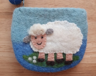 May include: A blue felt coin purse with a white felt sheep applique. The sheep has a smiling face and is standing on a green felt leaf with white felt flowers.