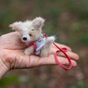 May include: A small, white and brown knitted dog toy with a red leash. The dog is wearing a pink and white knitted vest.