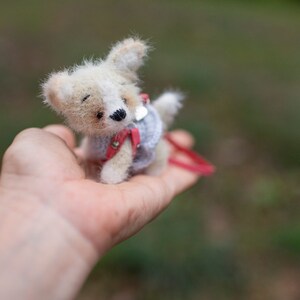 May include: A small, white and brown knitted toy dog wearing a red and gray sweater. The dog is being held in a person's hand.