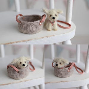 May include: A miniature, fluffy white dog with a pink collar and leash sits next to a small, crocheted basket with pink leather handles. The dog is positioned on a white chair, suggesting a pet accessory.