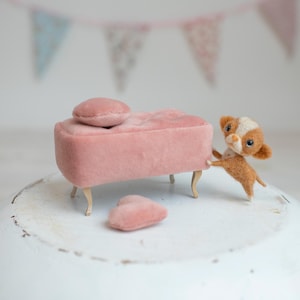 May include: A miniature pink velvet chaise lounge with a matching pillow and heart-shaped cushion. A small, brown and white dog figurine is playfully interacting with the furniture. The scene is set against a backdrop of pastel-colored bunting.