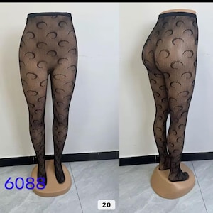May include: Black patterned tights with a crescent moon design. The tights are displayed on a mannequin leg, showcasing the full length and fit. The tights have a fishnet-like texture with the crescent moon pattern.