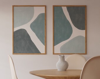 May include: Two framed abstract art prints in a light blue and white colour scheme. The prints are hanging on a white wall above a wooden table with a white ceramic vase and two beige chairs.