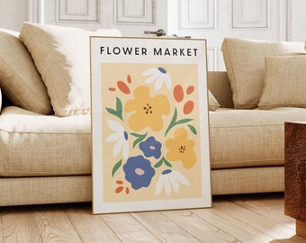 May include: A framed print with the text "FLOWER MARKET" at the top. The print features a colorful abstract floral design with yellow, blue, white, orange, and green flowers on a light yellow background.
