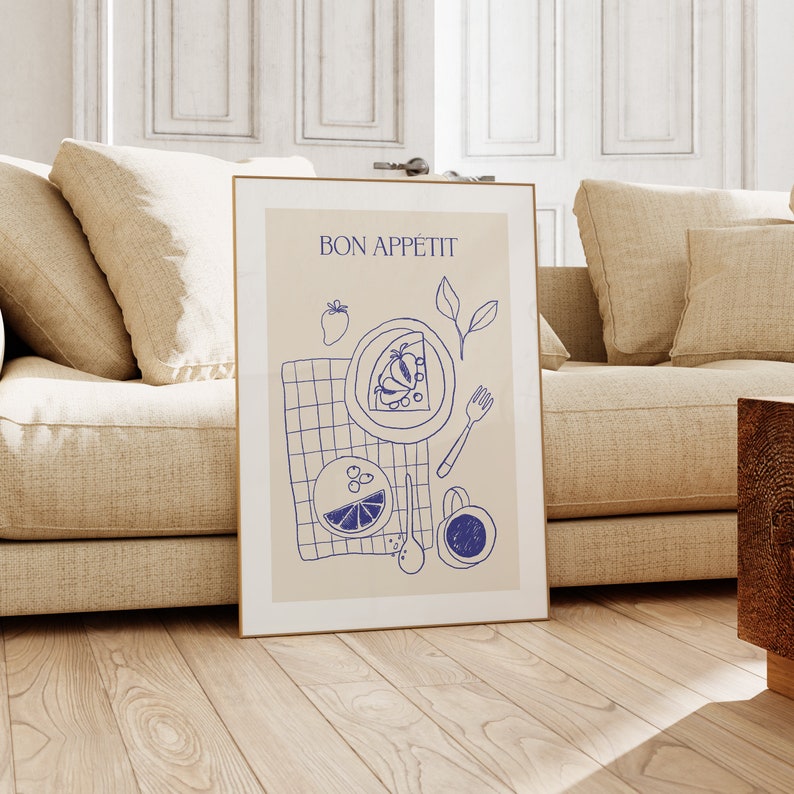 May include: A framed print with a beige background and blue line drawings of food and a checkered tablecloth. The text "BON APP&Eacute;TIT" is at the top of the print.