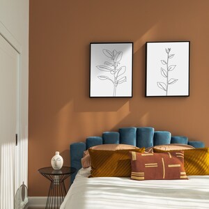 May include: A teal blue velvet headboard with a scalloped design. The headboard is decorated with a brown and gold patterned pillow and a white pillow with a brown geometric design. Two black framed prints with line drawings of plants hang on the wall behind the bed.