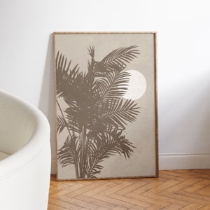 Op de afbeelding: Een ingelijst print met een beige achtergrond met een silhouet van palmbomen en een witte cirkel. De print heeft een lichtbruine lijst.