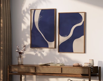 May include: Two framed abstract art prints with a blue and beige colour scheme. The prints are hanging on a white wall above a wooden console table.