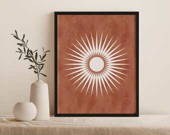 May include: A framed print with a white sunburst design on a terracotta background. The sunburst has a white circle in the center.