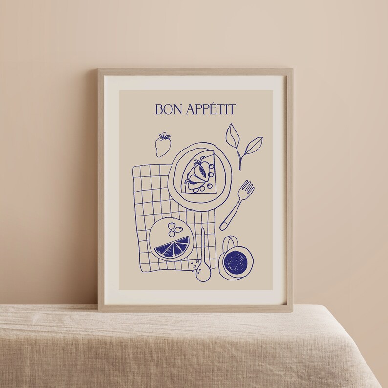 May include: A framed print with a beige background and blue line drawings of a plate of fruit, a glass of juice, a fork, a spoon, and a cup. The text "BON APP&Eacute;TIT" is at the top of the print.