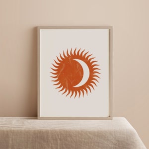 May include: A framed print with a minimalist design featuring a stylized sun and moon in a burnt orange color.