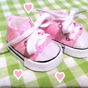 May include: A pair of pink canvas sneakers with white laces and white polka dots. The sneakers are on a green and white checkered background.