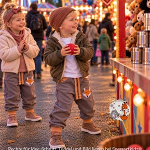 May include: Two children wearing grey corduroy joggers with fox face appliques, beige and olive jackets, and knit hats. The joggers feature drawstring waists and orange cuffs. A logo with a fox and rabbit illustration includes the text Spessartkidz.
