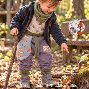 May include: A child wearing a dark blue fleece jacket, a light-colored shirt with a tree pattern, a green neck warmer, and purple corduroy pants with a fox-patterned pocket. The pants feature a patch with the text kleiner R&Auml;UBER.