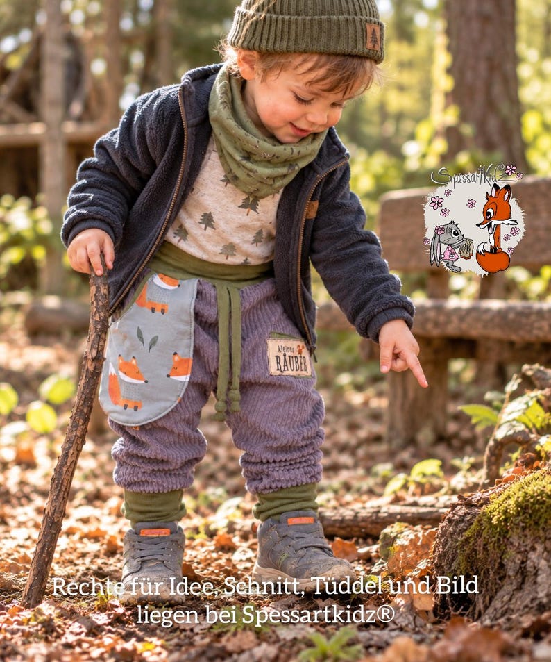 May include: A child wearing a dark blue fleece jacket, a light-colored shirt with a tree pattern, a green neck warmer, and purple corduroy pants with a fox-patterned pocket. The pants feature a patch with the text kleiner R&Auml;UBER.