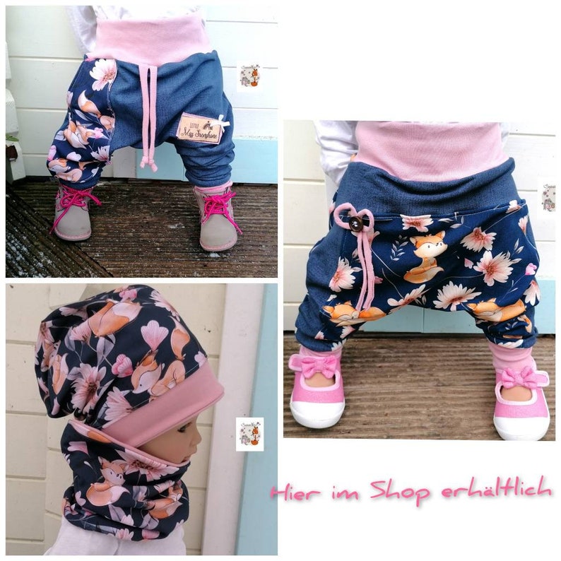 May include: A set of baby clothes featuring a blue and pink patterned fabric with a fox design. The set includes a pair of pants, a hat, and a scarf. The pants have a pink elastic waistband and a drawstring. The hat and scarf are both made of the same fabric as the pants. The text "Hier im Shop erh&auml;ltlich" is visible in the image.