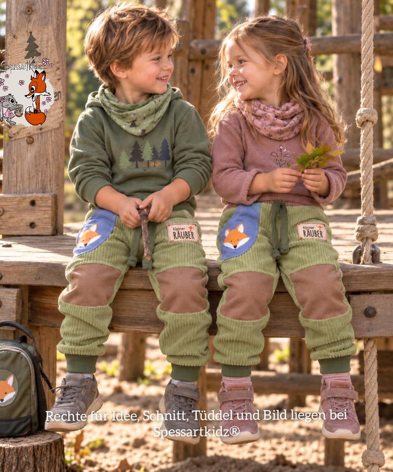 May include: Two children wearing olive green and dusty rose long-sleeve shirts with matching neck warmers and light green corduroy pants. The pants feature blue pockets with fox illustrations and patches labeled Kleiner R&auml;uber.