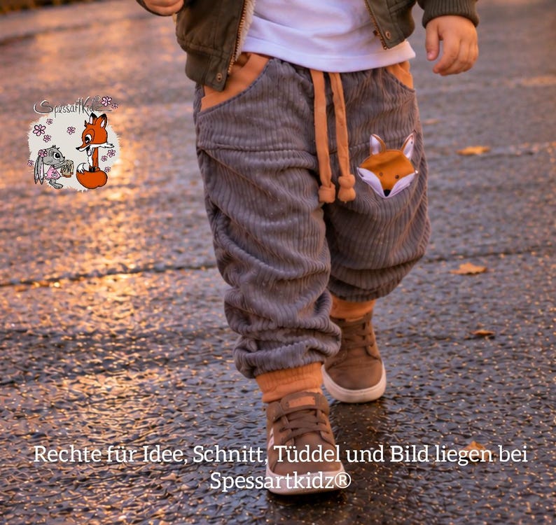 May include: Gray corduroy pants featuring a drawstring waist, orange trim at the pockets and cuffs, and a fox graphic on the left pocket. The pants are worn with a white shirt, a dark jacket, and brown sneakers. Text reads SpessartKidz.