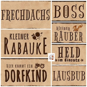 May include: A set of ten brown and white rectangular signs with various German phrases, including "Frechdachs", "Kleiner Boss", "Kleiner R&auml;uber", "R&auml;ubauke", "Held im Einsatz", and "Lausbub".