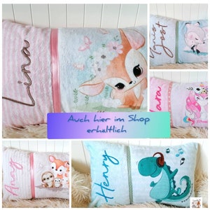 May include: A collection of personalized pillow covers with various animal designs. The pillows feature a pink and white striped fabric with a pink satin ribbon. The designs include a deer, a unicorn, a sloth, and a dinosaur. The pillows are embroidered with names such as "Anna", "Henry", "Laura", and "Janis Joest".