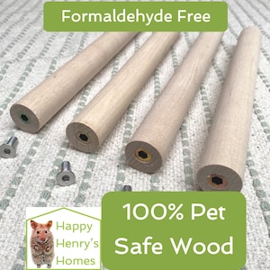 Peut inclure: Quatre chevilles en bois avec une finition naturelle et un trou percé à chaque extrémité. Les chevilles sont sur un tissu à motifs blancs et verts. Le texte "Formaldehyde Free" est en lettres vertes sur fond blanc. Le texte "100% Pet Safe Wood" est en lettres blanches sur fond vert. Le texte "Happy Henry's Homes" est en lettres blanches sur fond vert. L'image montre également deux vis argentées.