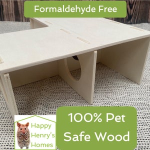 Könnte beinhalten: Ein weißes Holzhaus für Hamster mit zwei Eingängen und einer kleinen Öffnung in der Mitte. Das Haus ist aus 100% tiersicherem Holz gefertigt und frei von Formaldehyd. Der Text "Happy Henry's Homes" befindet sich in der linken unteren Ecke des Bildes.