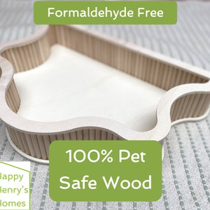 Puede incluir: Una cama de madera clara para mascotas con una forma única. La cama está hecha de madera natural y presenta el texto "Formaldehyde Free" y "100% Pet Safe Wood". Diseñada para mascotas pequeñas.