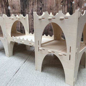 May include: A wooden playset for children, featuring a bridge, two towers, and a slide. The towers have arched openings and are made of unfinished wood.
