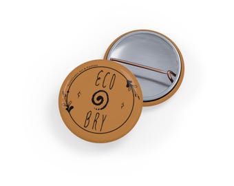 Könnte beinhalten: Zwei runde, hellbraune Buttons mit schwarzem Text und Designs. Ein Button zeigt die Worte "ECO BRY" in einem Spiraldesign. Der andere Button ist mit der Rückseite nach unten und zeigt die Anstecknadel. Die Buttons stammen von "Sustainable Art & Fashion".