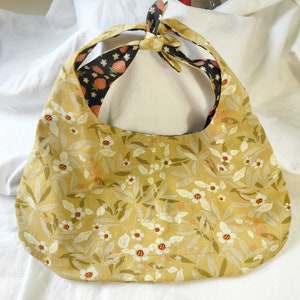 May include: A yellow fabric tote bag with a floral pattern. The bag has a black and white fabric lining with a strawberry print. The bag has a tie closure.