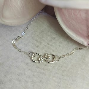 May include: A silver infinity symbol charm necklace with a small heart charm. The necklace is on a delicate silver chain.