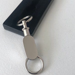 May include: A silver key chain with a swiveling oval-shaped tag. The tag has a smooth, polished surface.