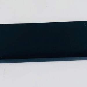 May include: A rectangular, black box with a glossy finish. The box is set against a white background. The box is a simple, sleek design, suitable for packaging or storage.
