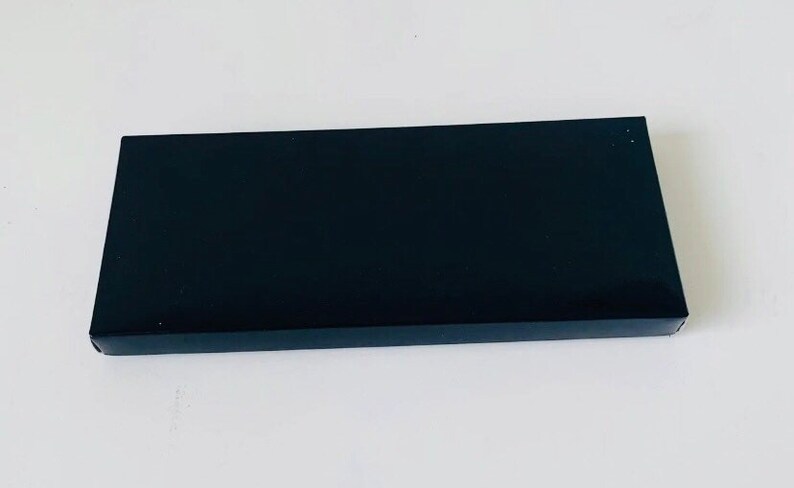 May include: A rectangular, black box with a glossy finish. The box is set against a white background. The box is a simple, sleek design, suitable for packaging or storage.